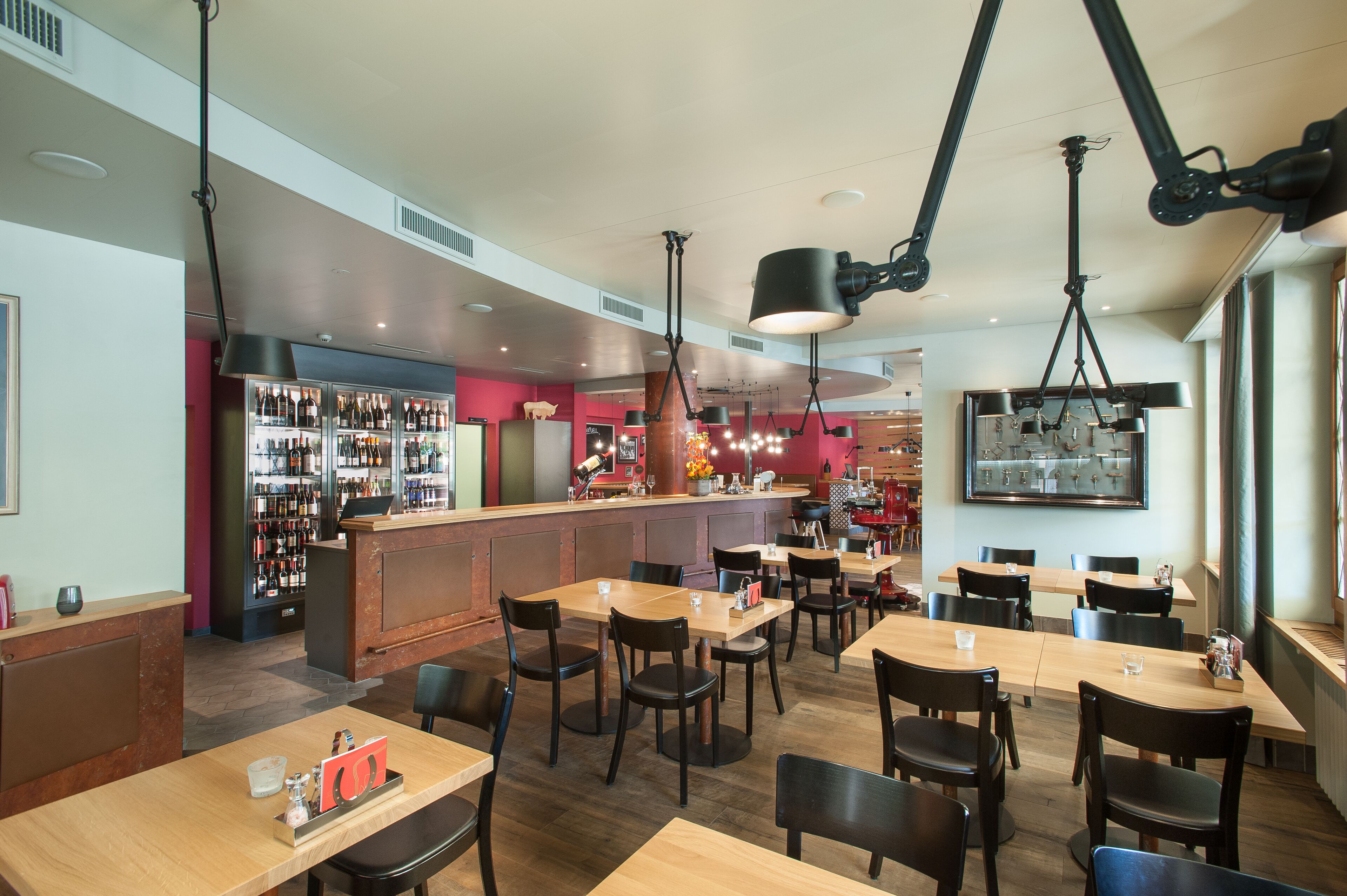 A restaurant with multiple tables and chairs, a bar area with a wine display, and hanging pendant lights.
