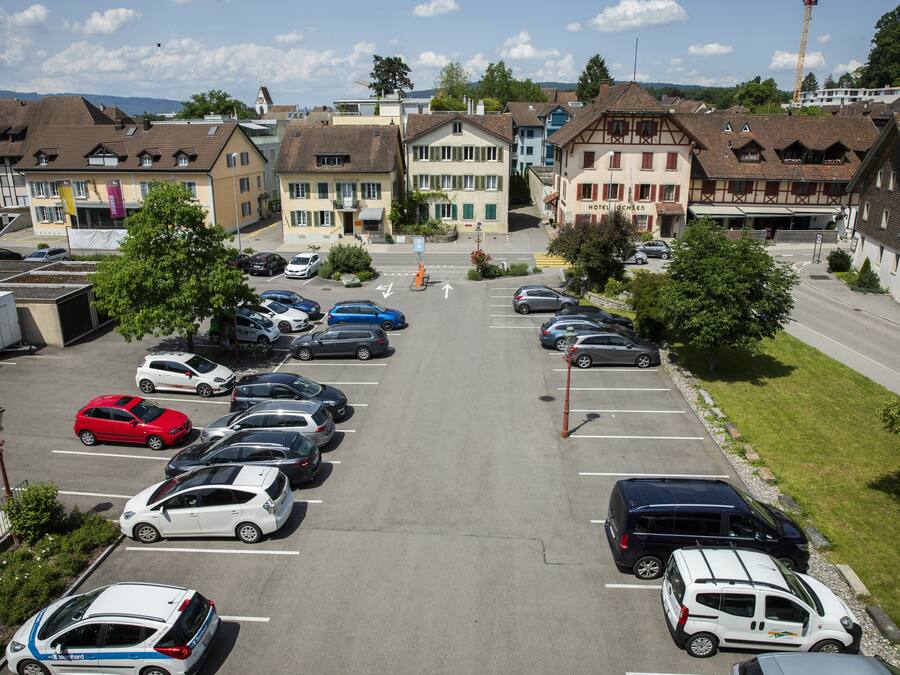 Un estacionamiento con varios autos, un edificio de hotel y una grúa al fondo.