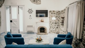 Una sala de estar con chimenea, paredes de piedra, un televisor y dos sofás azules.