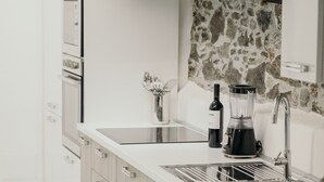 Una cocina moderna con armarios blancos, salpicadero de piedra, horno empotrado y encimera con una botella de vino y una licuadora.
