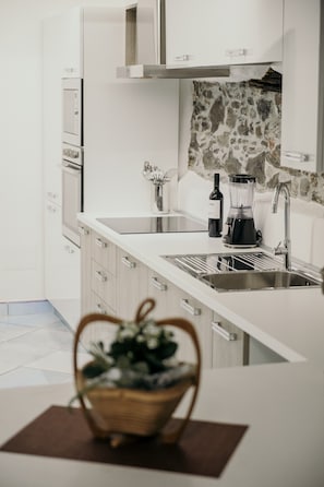 A modern kitchen with white cabinetry, a stone backsplash, a built-in oven, and a countertop with a wine bottle and blender.