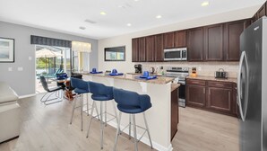 A modern kitchen with dark wood cabinets, stainless steel appliances, and a bar area with blue stools. - Stunning villa, lake views-south facing pool - game room,  near Disney & golf (Davenport)