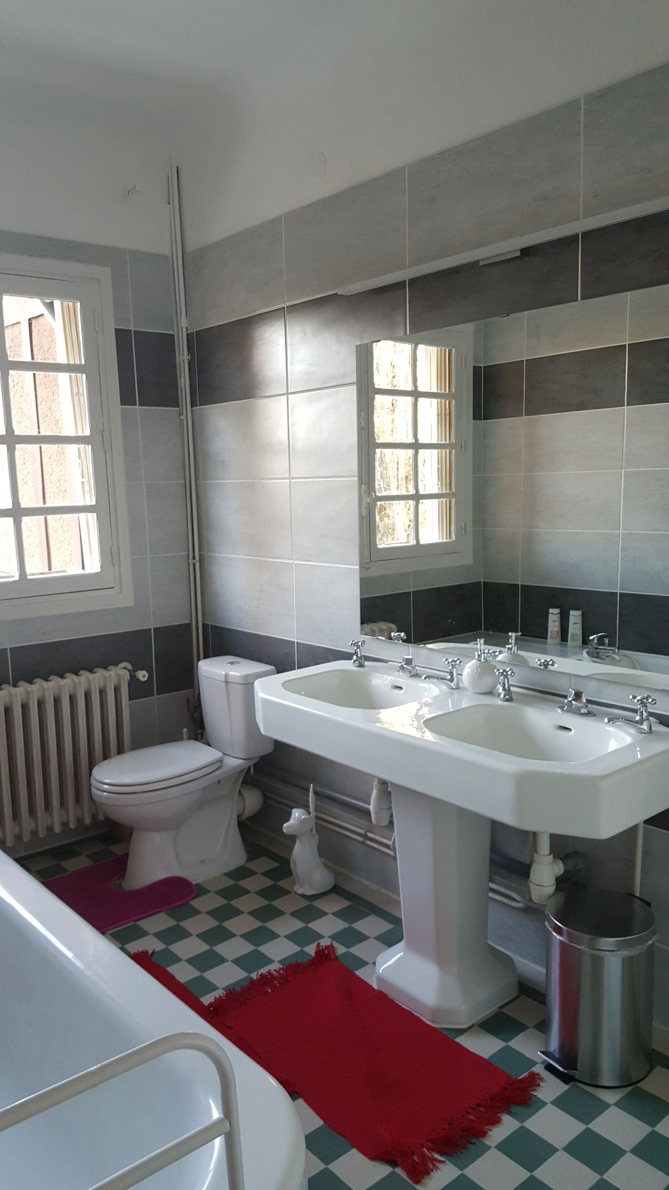 A bathroom with a toilet, bidet, sink, and a red rug.