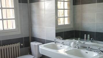 A bathroom with a toilet, bidet, sink, and a red rug.