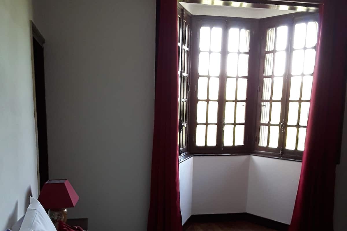 Une chambre avec un grand lit, une fenêtre avec des rideaux rouges et un plancher en bois.