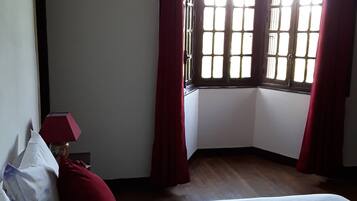 A bedroom with a large bed, a window with red curtains, and a wooden floor.