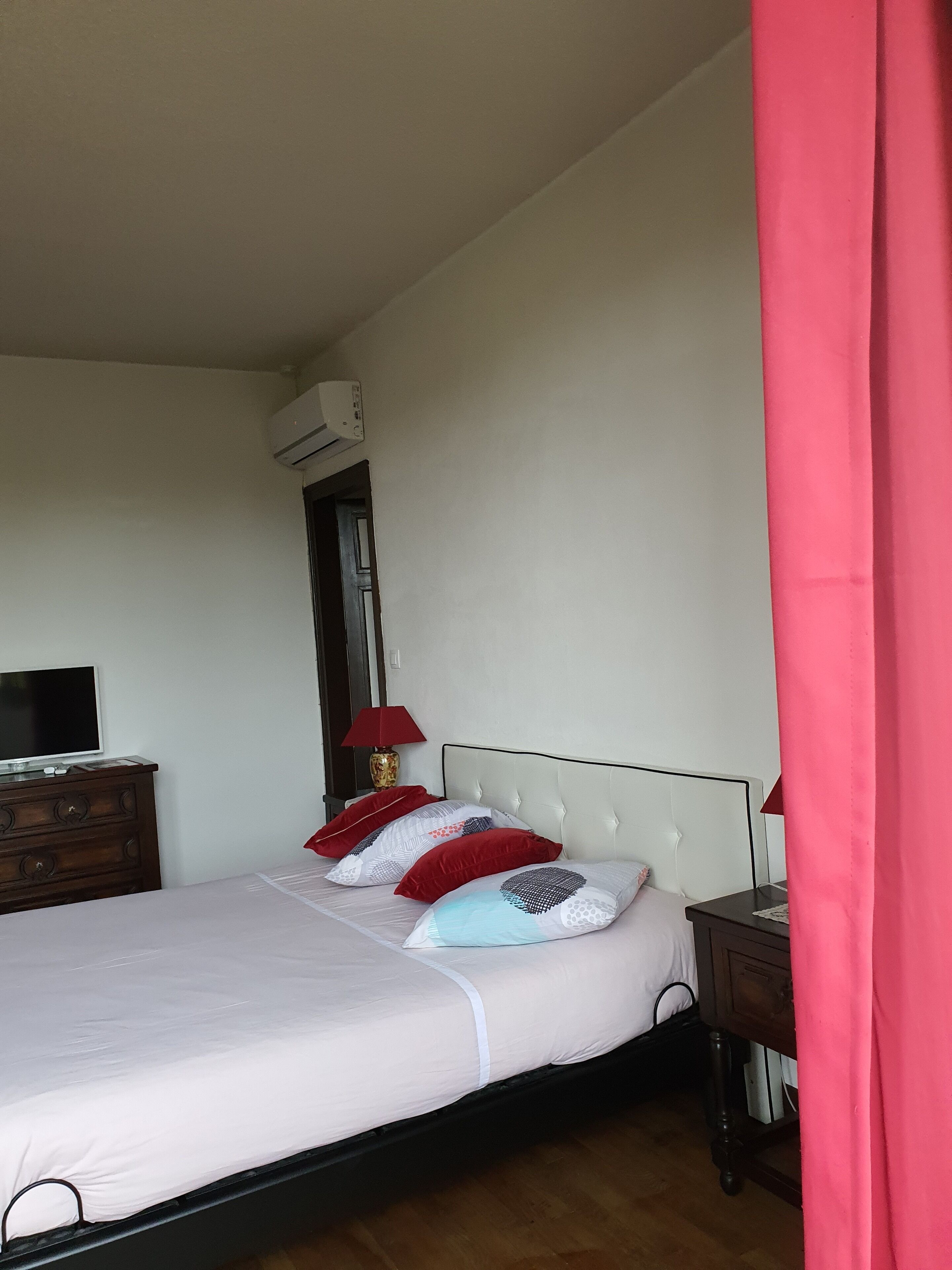 A bedroom with a bed, a TV on a dresser, a lamp, and an air conditioning unit.