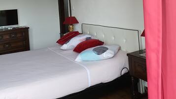 A bedroom with a bed, a TV on a dresser, a lamp, and an air conditioning unit.