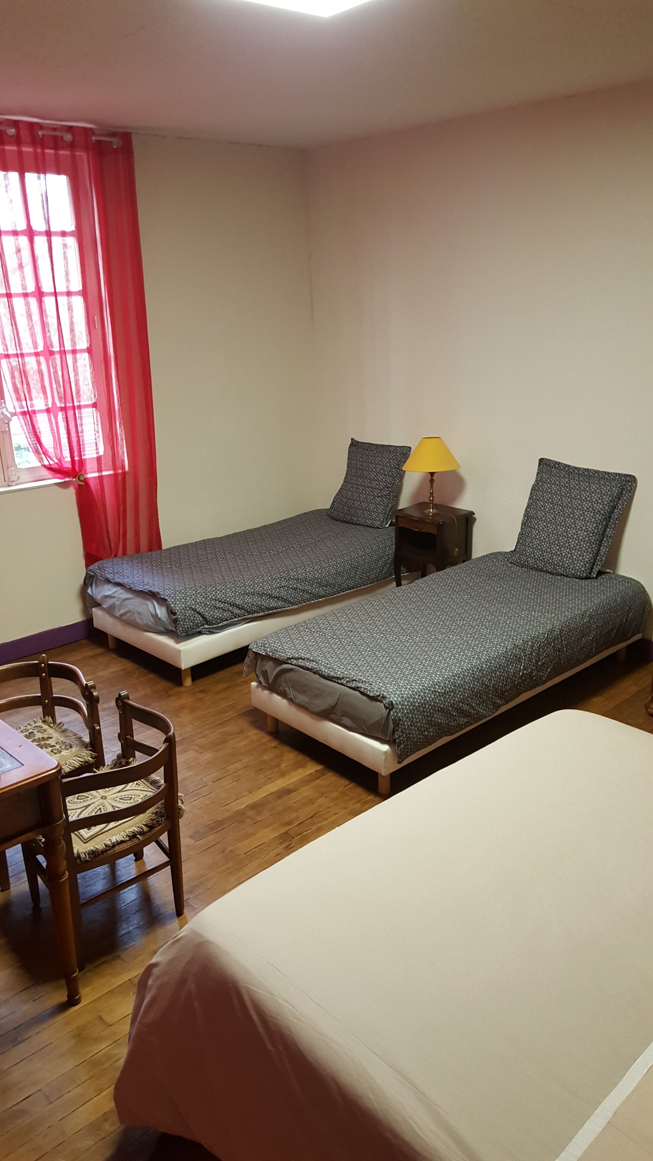 A room with two single beds, a small table, a chair, and a lamp.