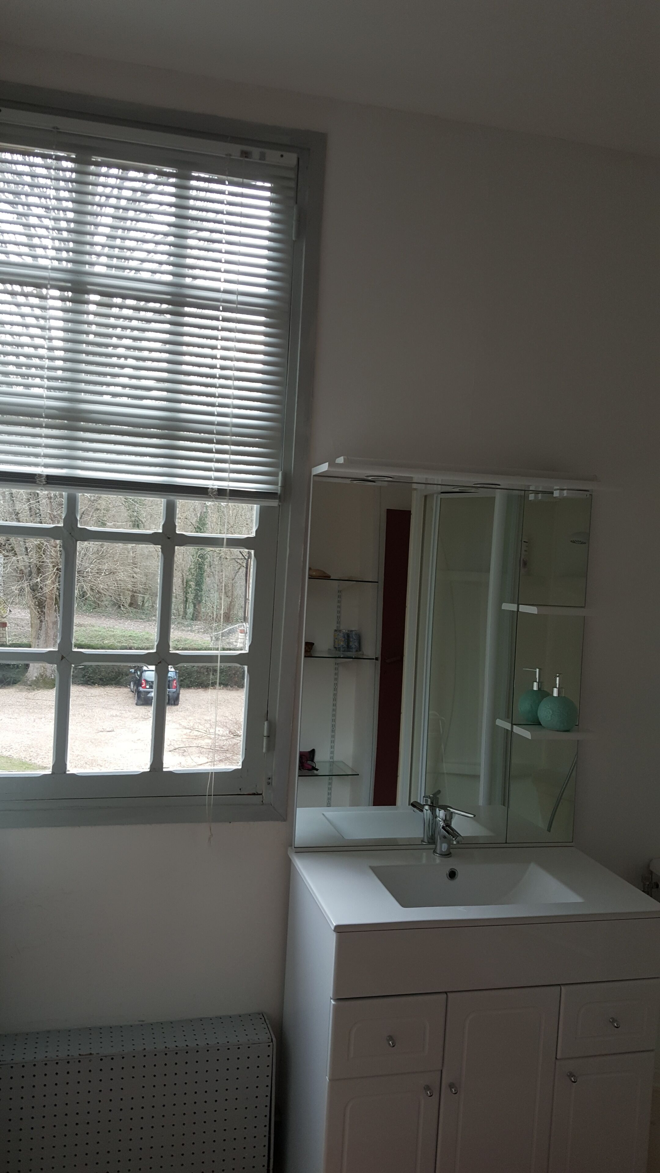 A bathroom with a window, a sink, a mirror, and a cabinet.