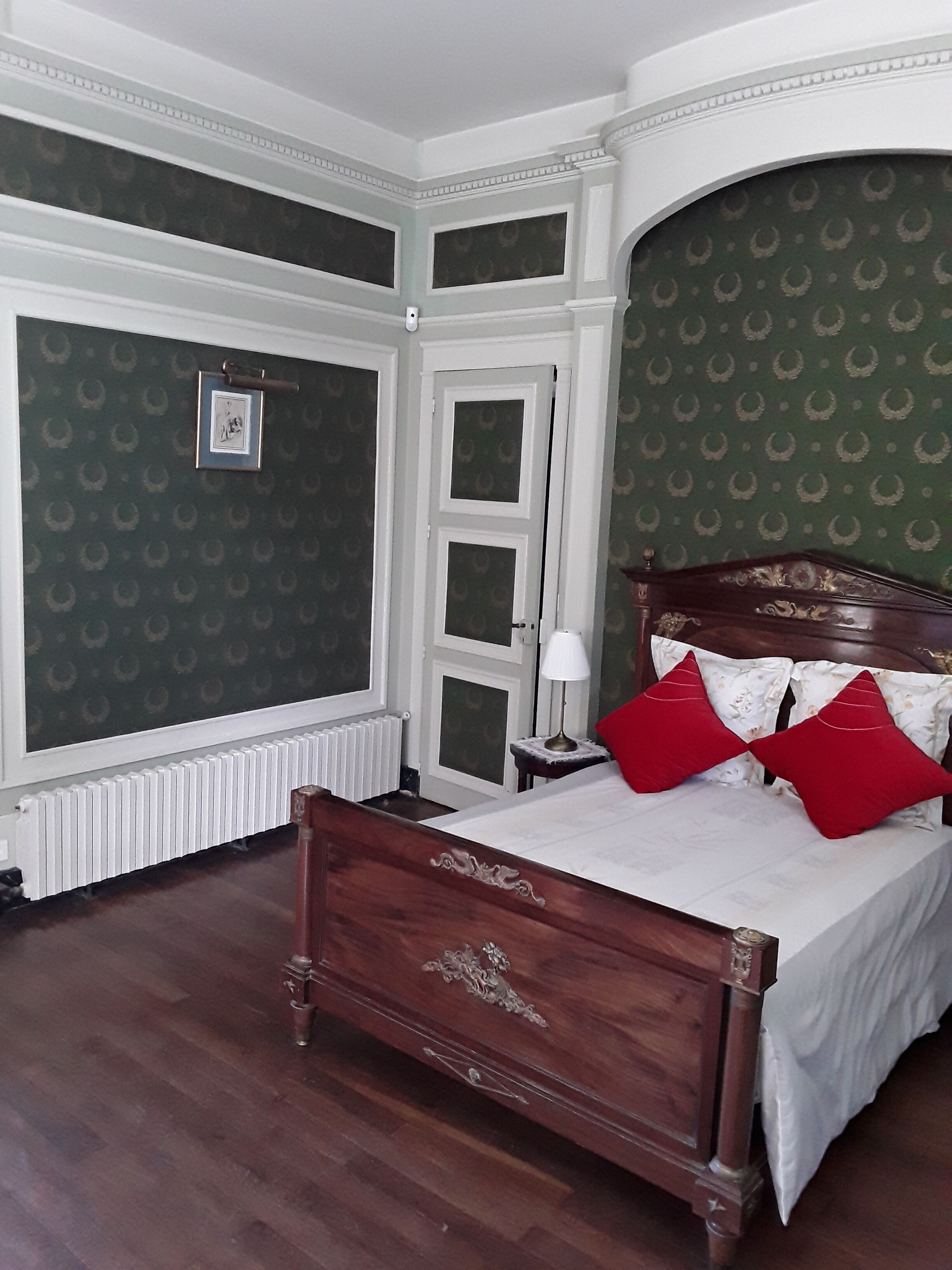 Une chambre à coucher classique avec un lit en bois, un papier peint à motifs verts et un radiateur blanc.