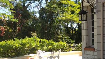 An outdoor patio with a round table and white chairs, surrounded by greenery and trees.