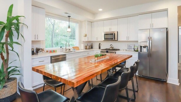 Una cocina moderna con armarios blancos, una isla de madera, sillas negras y un refrigerador de acero inoxidable.