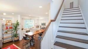 Una cocina moderna con una isla central, una escalera de madera y un comedor con sillas.
