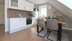 A modern kitchen with white cabinets, a built-in oven, and a dining area with two chairs and a wooden table. - Apartment Hafenbrise in Greetsiel for 4 people (Greetsiel)