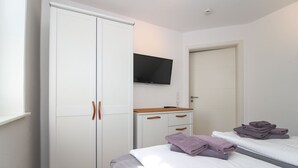 A bedroom with a wardrobe, a bedside table, a bed, and a television mounted on the wall. - Apartment Hafenbrise in Greetsiel for 4 people (Greetsiel)