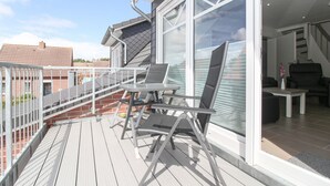 A balcony with a table and chairs, a view of the city, and a staircase leading to an upper floor. - Apartment Hafenbrise in Greetsiel for 4 people (Greetsiel)