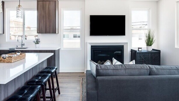 A modern kitchen with a central island, bar stools, a fireplace, and a large grey sofa in a living area. - Book now Summer is here— Pet,2BR/2BA, 2 Parking (Newport Beach)