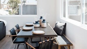 A dining area with a wooden table, black chairs, and a view of the outside through large windows. - Book now Summer is here— Pet,2BR/2BA, 2 Parking (Newport Beach)