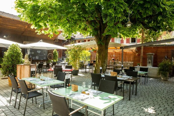 An outdoor cafe with tables and chairs, surrounded by trees and plants.