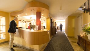 A hotel reception area with a curved wooden counter, a receptionist, and a man standing by the counter. - Gartenhaus by Ochsen Lenzburg (Lenzburg)