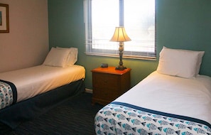 Een hotelkamer met twee bedden, een nachtkastje met een lamp en een raam met zonwering.