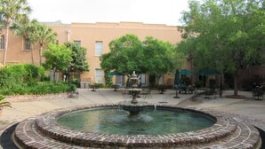 Une cour intérieure avec une fontaine circulaire en briques, entourée d’espaces aménagés pour s’asseoir et d’arbres.