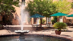 Une fontaine dans une cour dallée de briques, entourée de sièges extérieurs et de parasols.