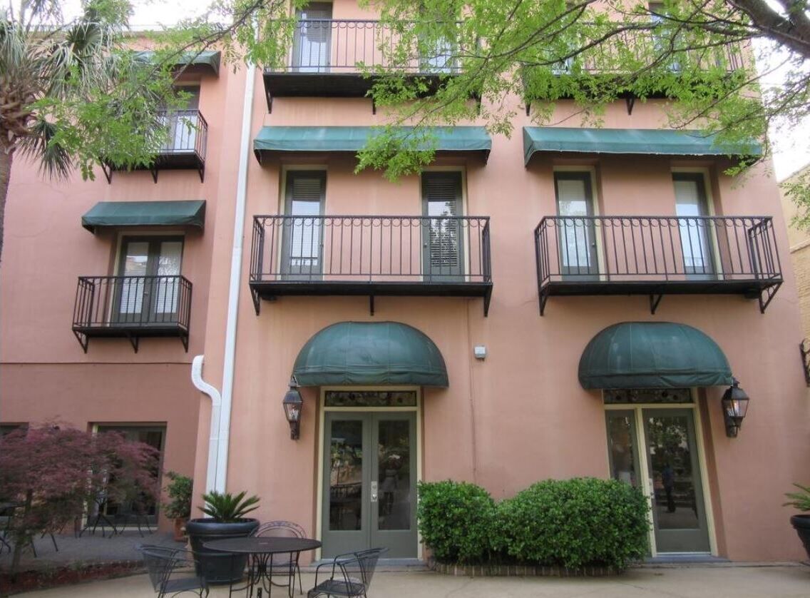 A multi-story building with balconies, green awnings over the doors, and outdoor seating.