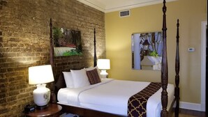 A four-poster bed with white linens, two bedside lamps, a brick wall, and a large window with a view of trees. - The Lodge Alley Inn in the heart of Charleston! (Charleston)