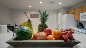 Una cocina con un frutero que contiene plátanos, manzanas, naranjas, uvas, una piña y una sandía.