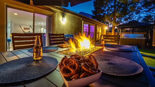 Un área de comedor al aire libre con una fogata, un bol de pretzels y una botella de cerveza.
