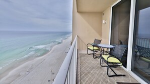 A balcony with a view of the beach and ocean. There are two chairs and a small table.