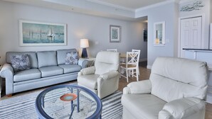 A living room with a grey sofa, white armchairs, a round coffee table, and a painting of sailboats.