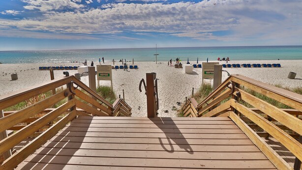 A wooden boardwalk leading to a sandy beach with a clear sky.