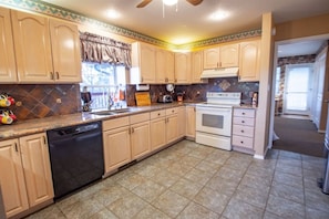 A kitchen with light wooden cabinets, a dishwasher, a stove, and a window with curtains. - Come Stay at Life`s a Hoot (Ruidoso)