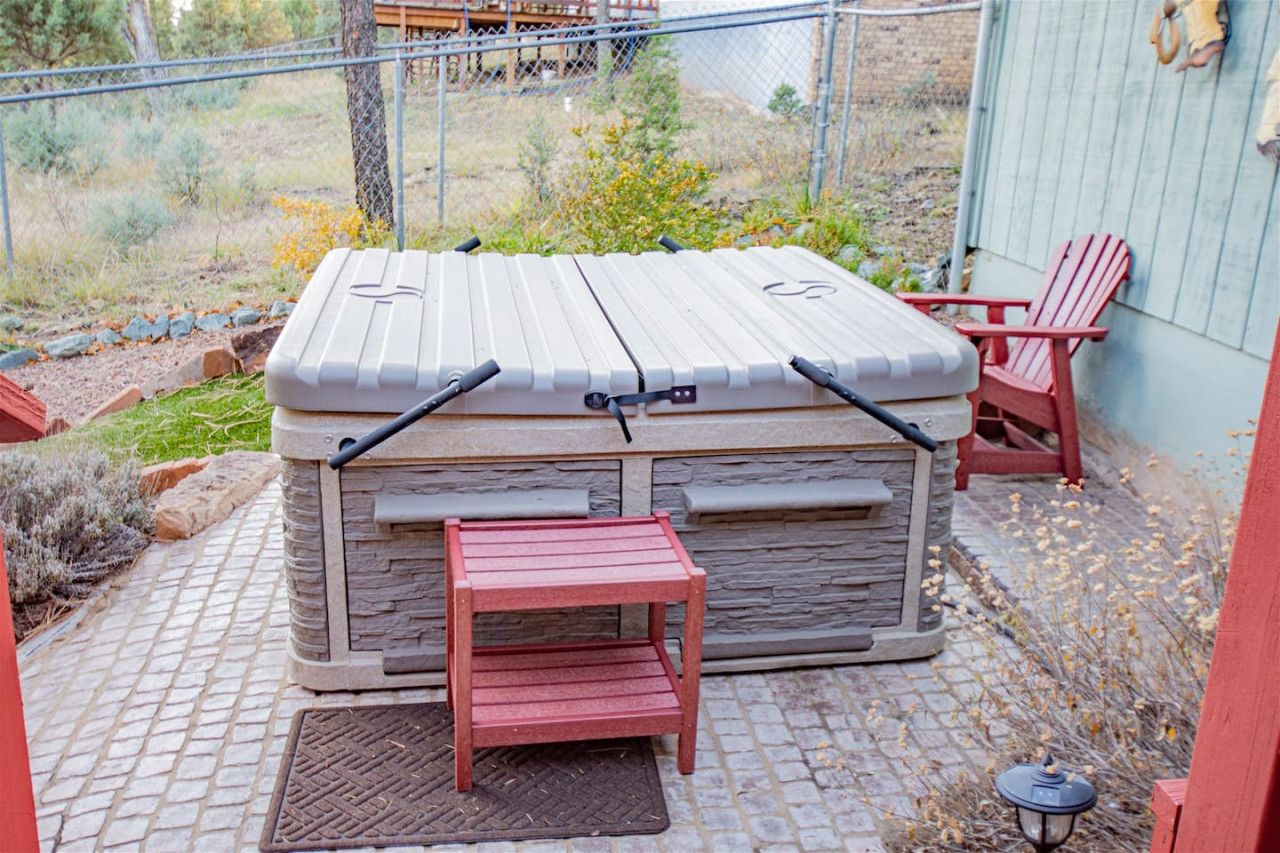 A stone hot tub with a wooden bench in front, a red chair, and a lantern on the patio.