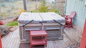 A stone hot tub with a wooden bench in front, a red chair, and a lantern on the patio.