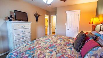 A bedroom with a patterned bedspread, a television on a dresser, a ceiling fan, and a door leading to another room.