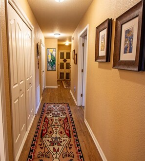 A hallway with a patterned rug, white doors, and framed artwork on the walls. - Come Stay at Life`s a Hoot (Ruidoso)