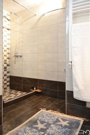 A modern bathroom with a shower, tiled walls, a patterned rug, and a towel rack.