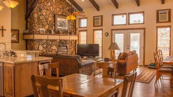 A spacious living area with a stone fireplace, wooden furniture, and large windows.