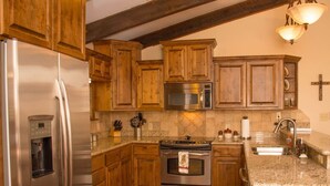 A kitchen with wooden cabinets, stainless steel appliances, granite countertops, and a cross on the wall. - Horsin` Around - Unit M2 (Ruidoso)