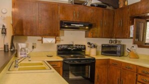 A kitchen with wooden cabinets, a stove, a microwave, and a sink. - Come Stay in Antlers - D4 (Ruidoso)