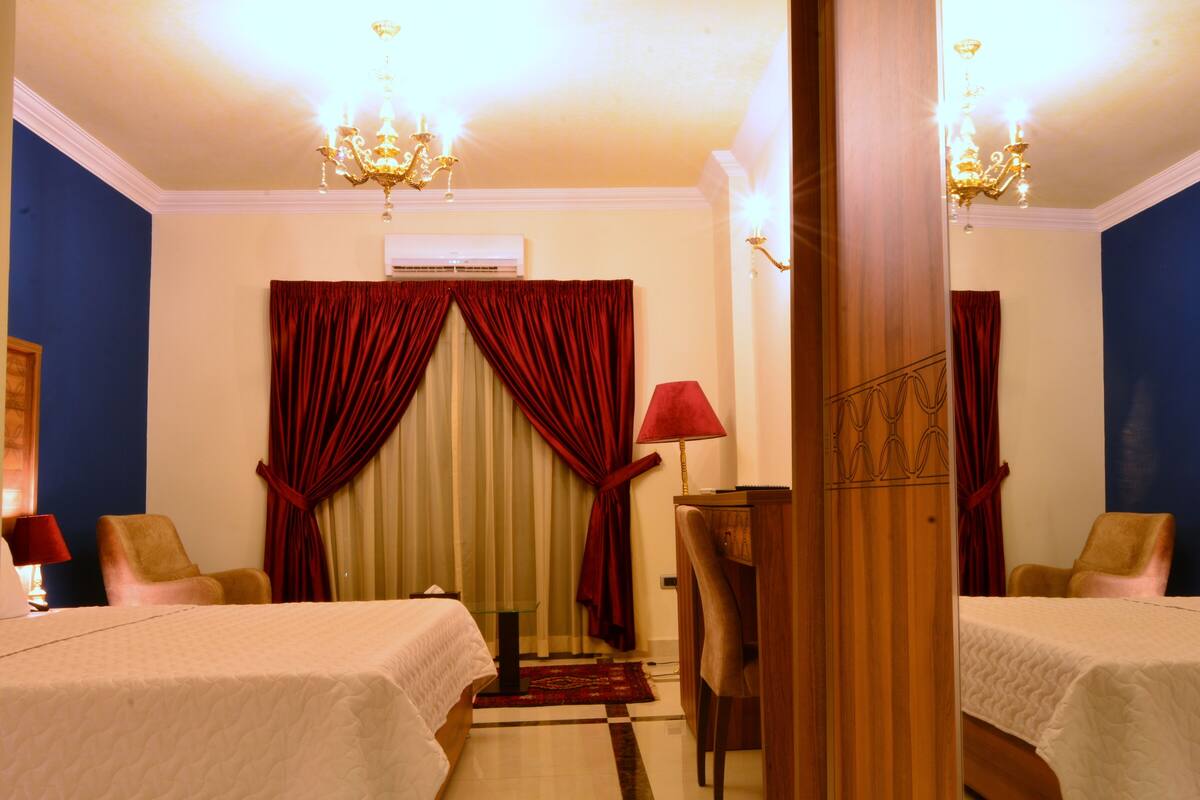Een hotelkamer met twee bedden, een kroonluchter, een rode lamp en een houten kast.