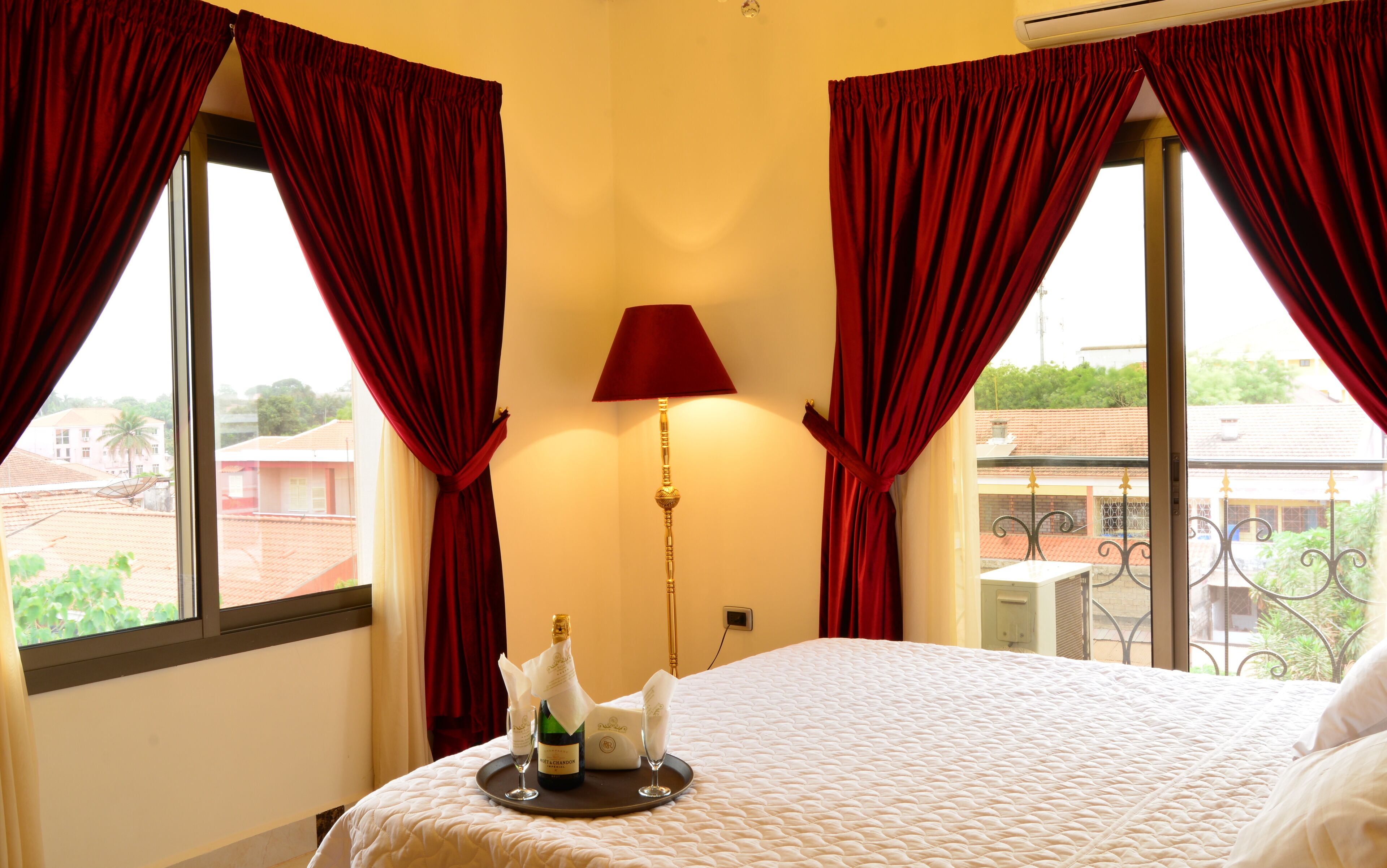 A hotel room with a bed, a table with a bottle of champagne, and red curtains.