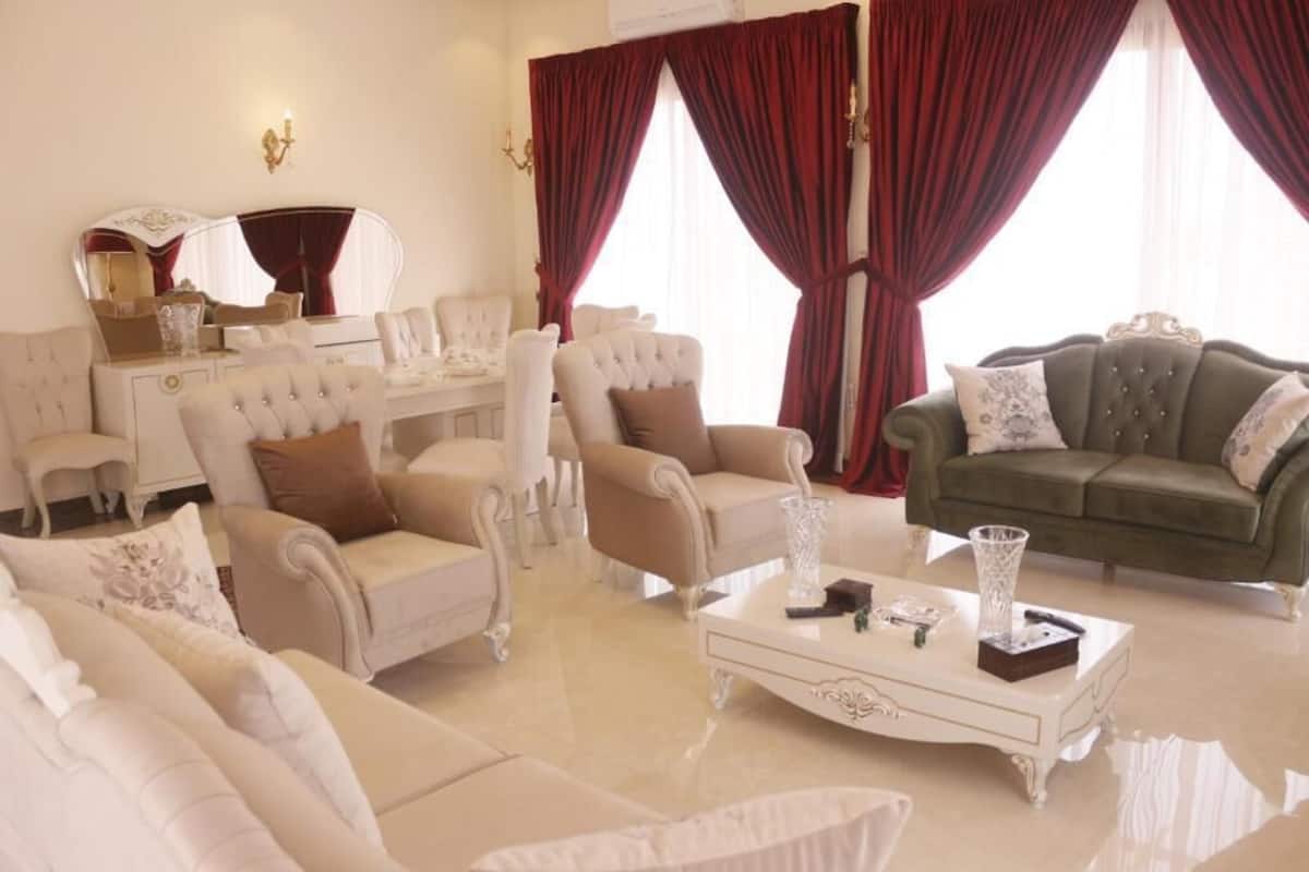 Een luxe woonkamer met een beigekleurige zithoek, een groene bank en een witte salontafel met decoratieve objecten.