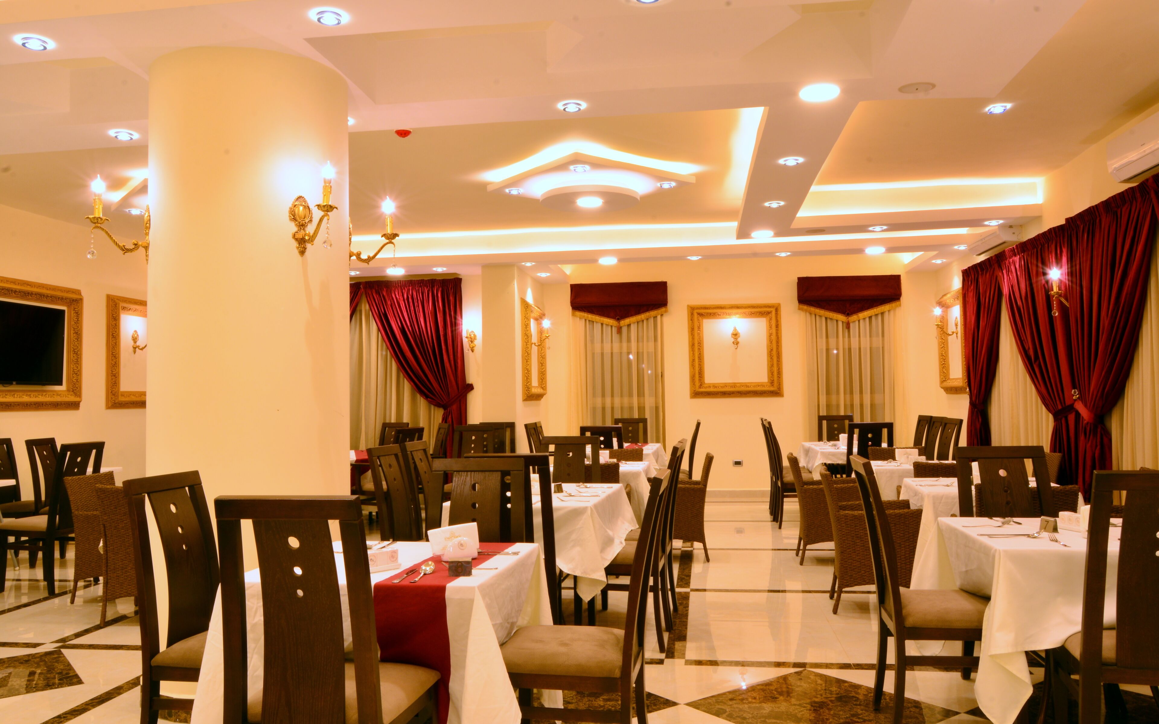 A restaurant with multiple tables and chairs, ceiling lights, and red curtains.
