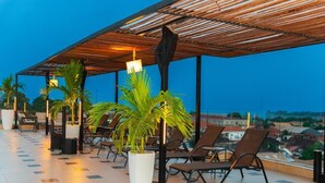 Terraza en la azotea con sillones de descanso, plantas en macetas y vistas de la ciudad.
