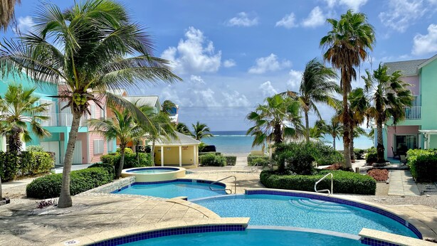 A pool area with multiple swimming pools, palm trees, and a view of the ocean.